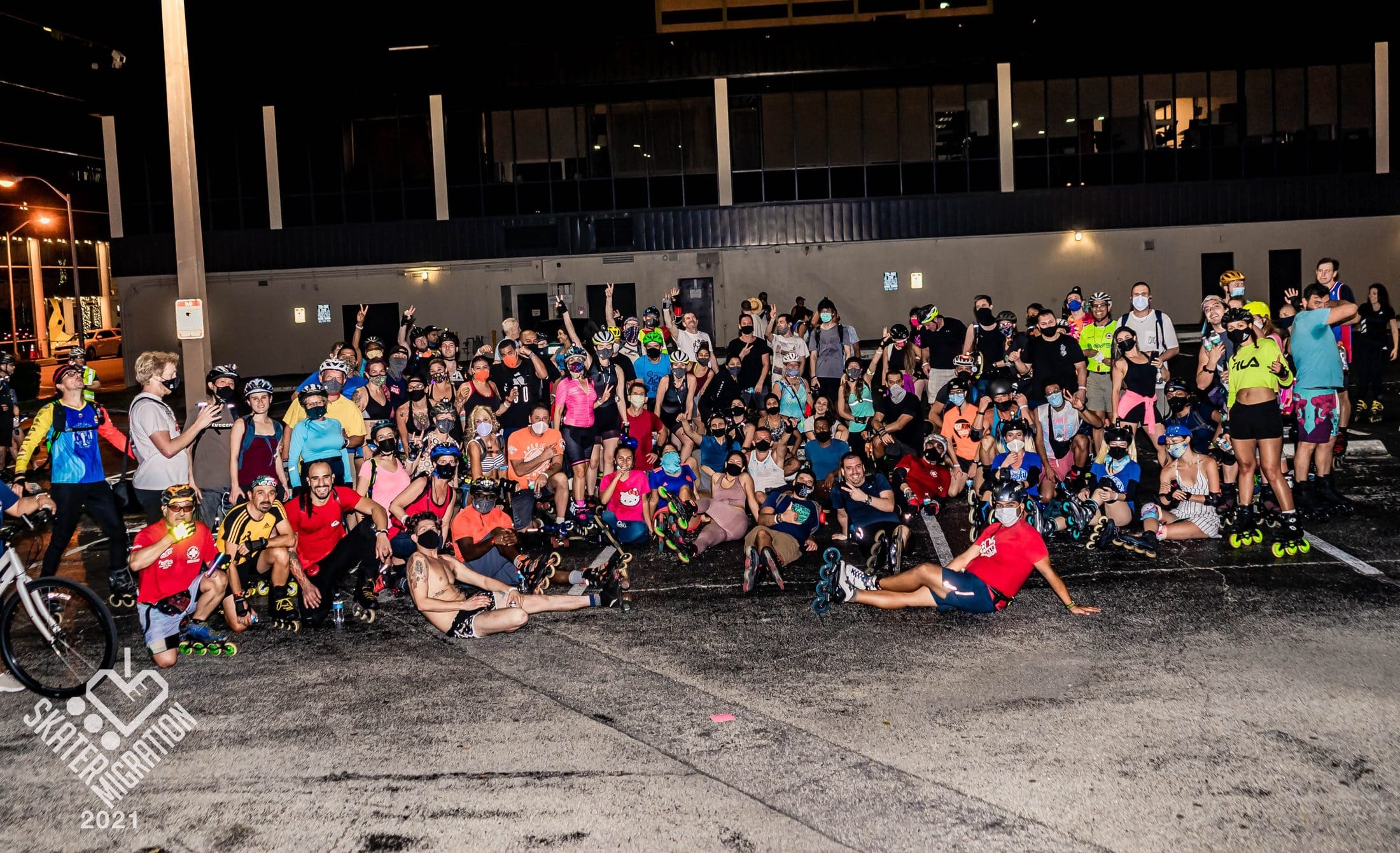 Dozens of skaters and cyclists sitting together during a night skate stop