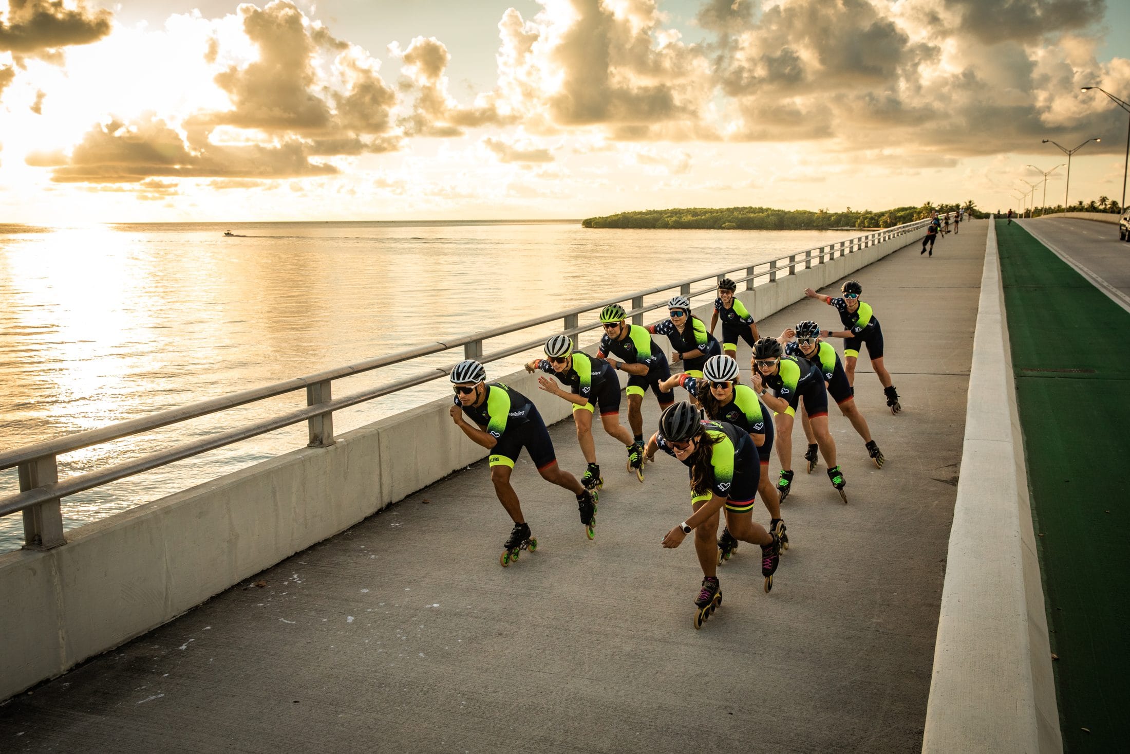SobeRollers skaters in navy and neon team kits skating in a paceline across a Miami causeway at golden hour