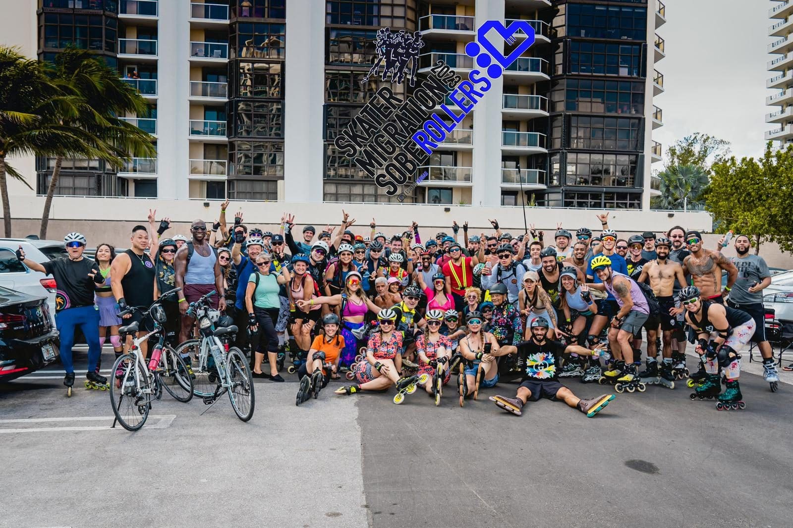 A huge group of skaters and cyclists posing in front of a Miami Beach tower