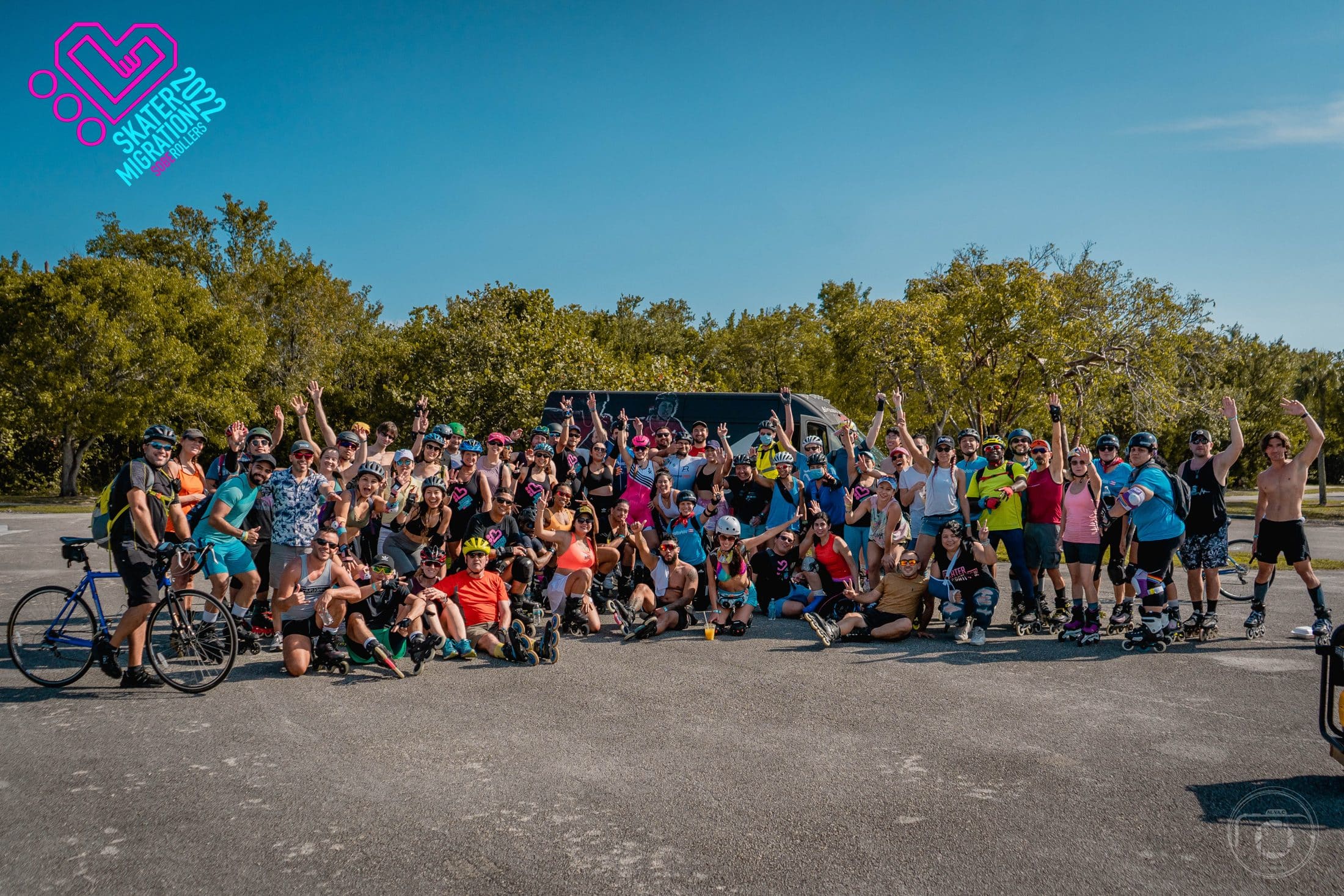 A large group of skaters and cyclists cheering in a park under a blue sky