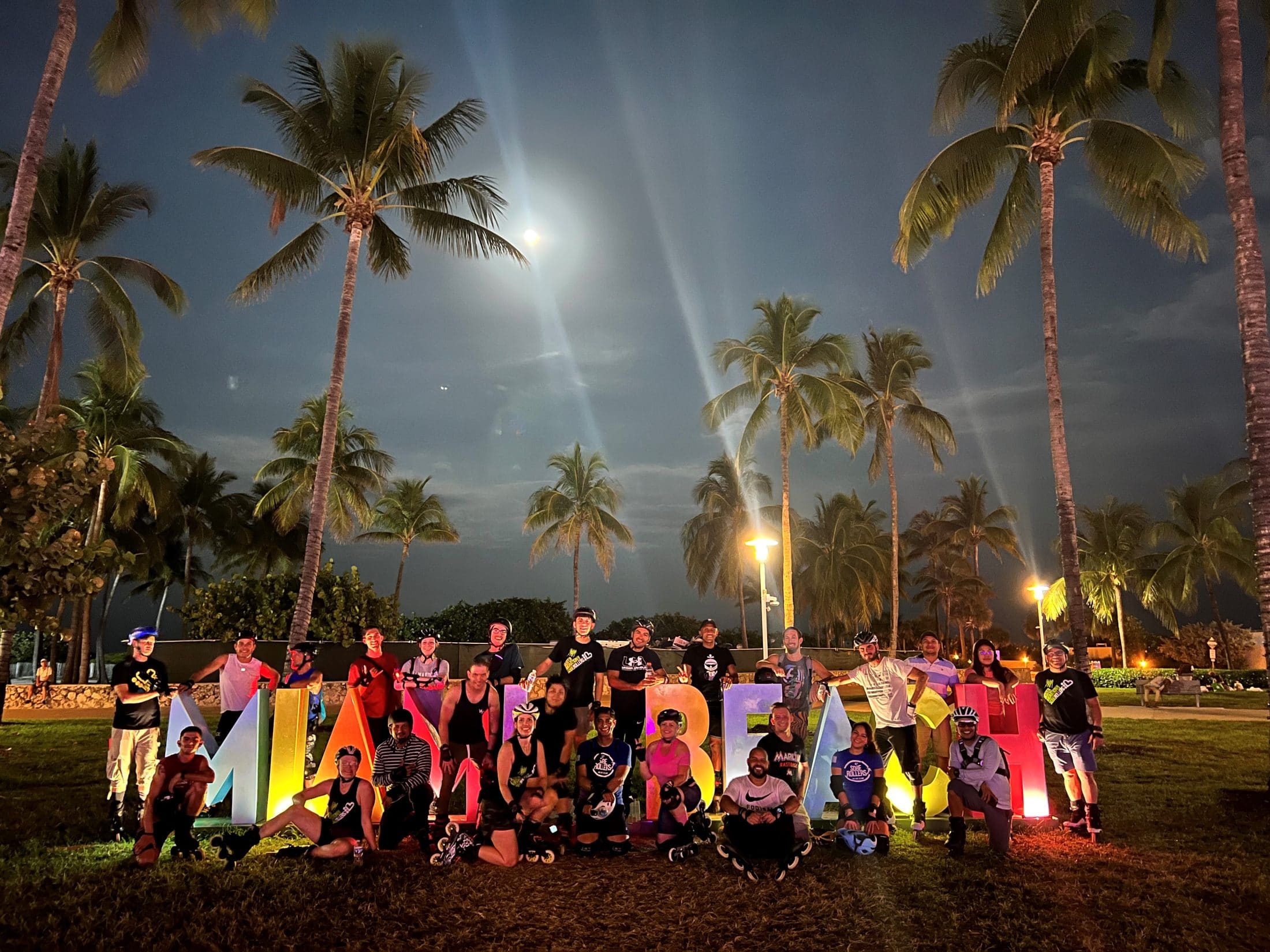 The group sitting around the giant illuminated Miami Beach letters under palm trees at night