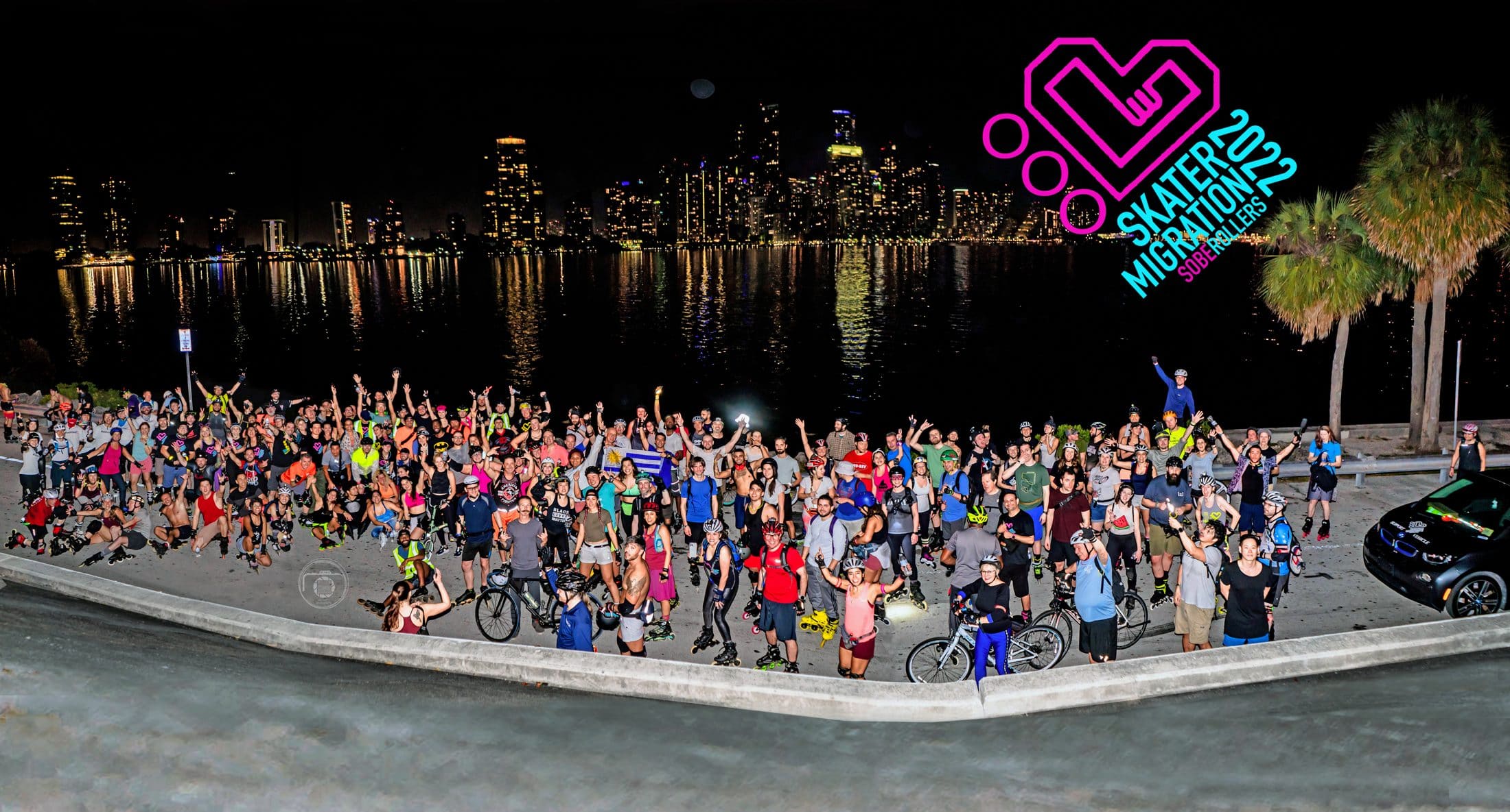 Hundreds of Skater Migration skaters cheering on the bay with the Miami skyline lit up behind them